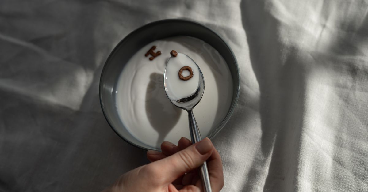 A close-up of a hand holding a spoon over a bowl of milk with letter-shaped cereals.